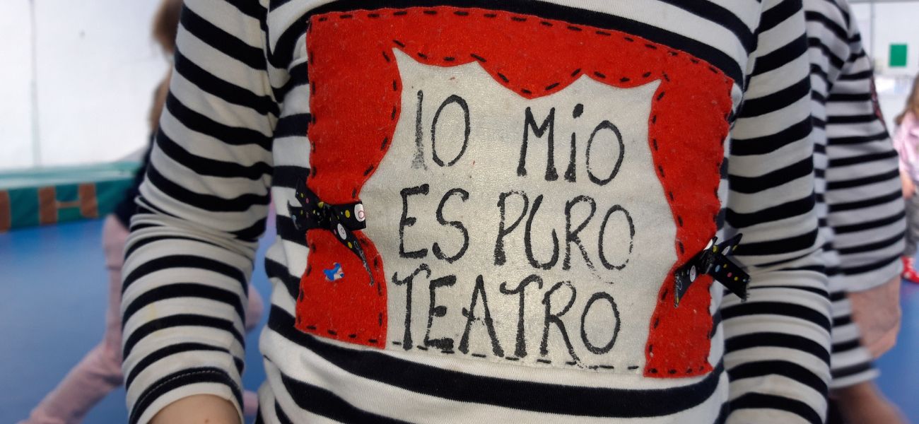 Una persona con una camiseta que tiene un dibujo de una obra de teatro con un telón rojo y tiene escrito en su interior "Lo mio es puro teatro"